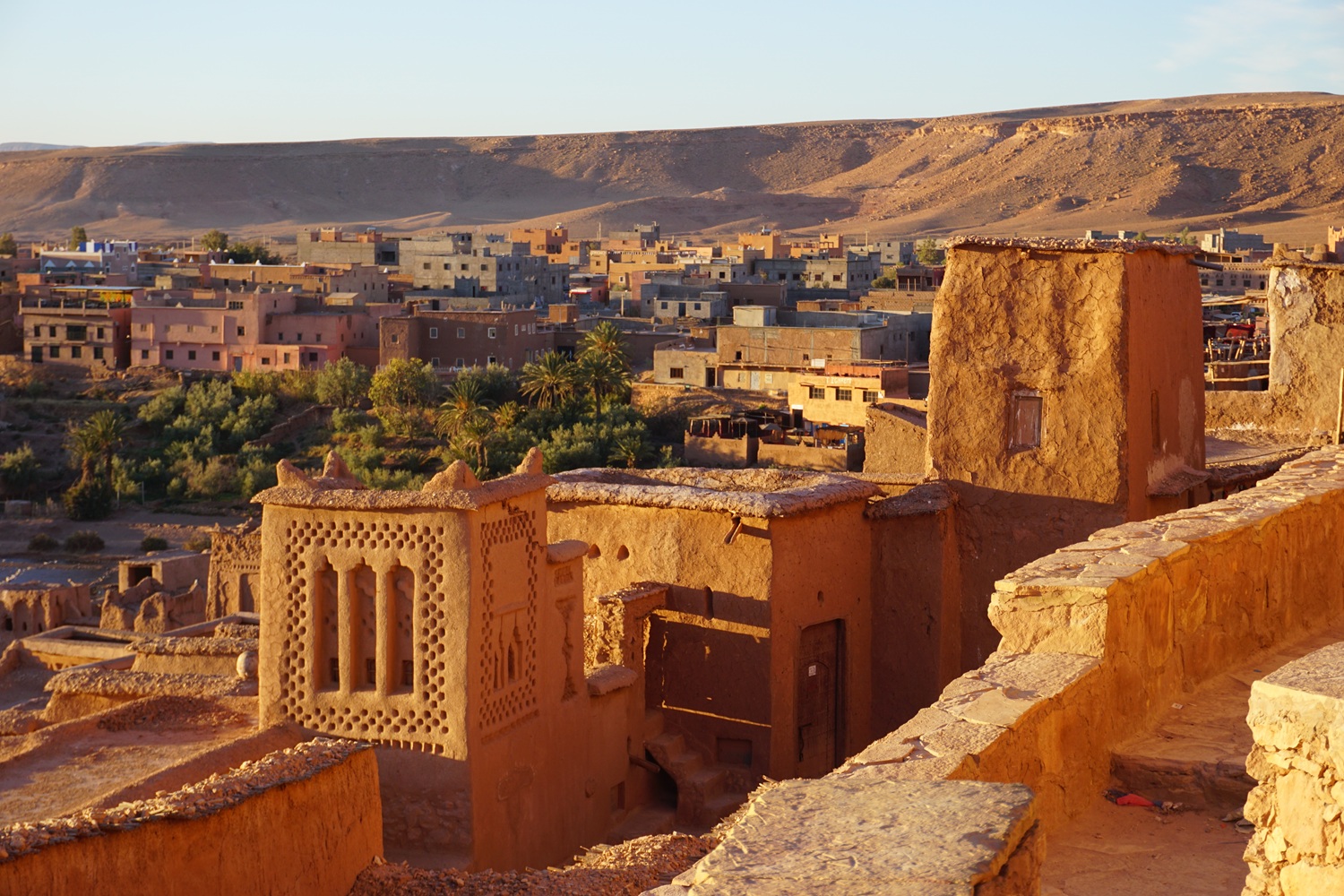Trekking route toward Ighrem Akdim oasis, with green gardens, earthen houses and remote High Atlas foothill landscapes.